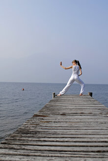 Italy, Lake Garda, Woman (20-25) exercising yoga on jetty - DKF00110