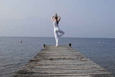 Italy, Lake Garda, Woman (20-25) exercising yoga on jetty - DKF00109