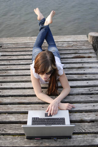 Italy, Lake Garda, Young woman (20-25) using laptop on dock, close-up stock photo