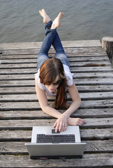 Italien, Gardasee, Junge Frau (20-25) mit Laptop auf Steg, Nahaufnahme - DKF00108