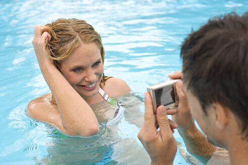 Young man photographing woman in pool - BABF00333