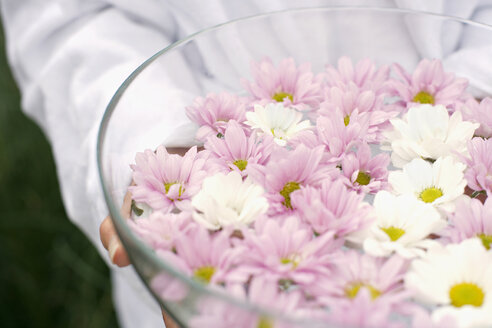 Woman holding bowl of petals in water, close-up, mid section - BABF00280