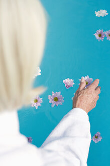 Germany, senior woman touching flower floating on surface of water - BABF00255