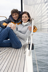 Germany, Baltic Sea, Lübecker Bucht, Young couple on sailing boat sitting and holding mugs - BAB00403