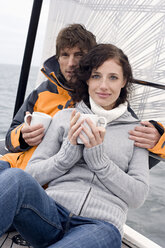 Germany, Baltic Sea, Lübecker Bucht, Young couple on sailing boat sitting and holding mugs, portrait - BAB00401