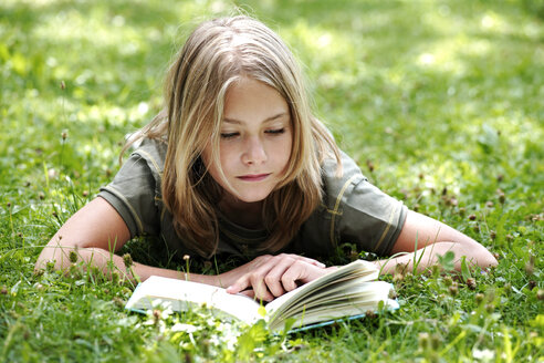 Girl (13-14) lying on grass reading, smiling - TCF00355