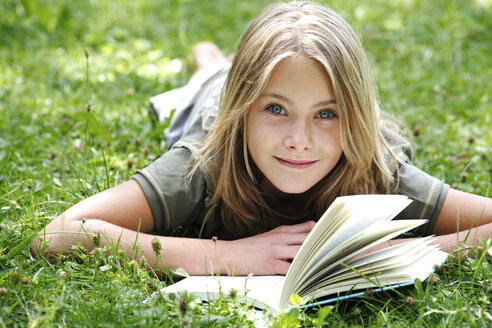Mädchen (13-14) liegt im Gras und liest, lächelt - TCF00354