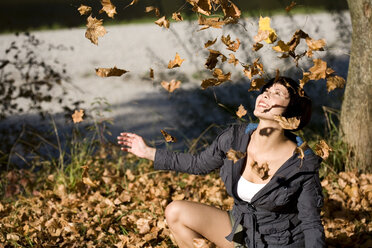 Germany, Bavaria, Young woman looking at falling Autumn leaves, portrait - MAEF00667