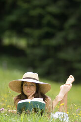 Young woman holding book, lying in meadow - HHF01758