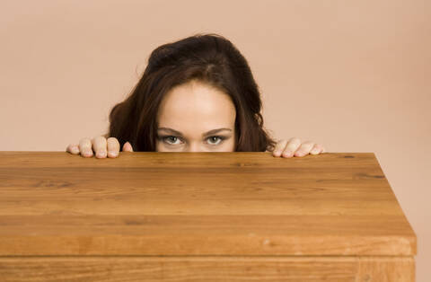 Junge Frau versteckt sich hinter einem Tisch, lizenzfreies Stockfoto