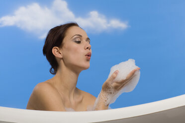 Young woman in bubble bath, blowing suds from hands, side view - RRF00015