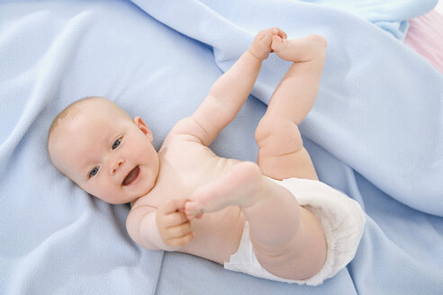 Baby boy (6-9 months) lying on bed, touching toes - SMOF00112