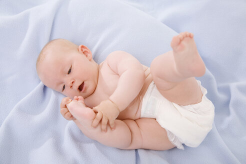 Baby boy (6-9 months) lying on bed touching toes - SMOF00111