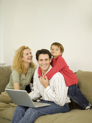 Young family in living room, father using laptop - WESTF06647