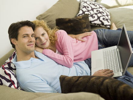 Junges Paar auf Sofa mit Laptop, lächelnd - WESTF06562
