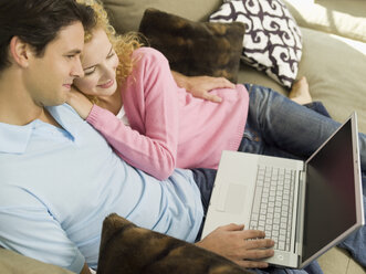 Young couple on sofa, man using laptop, smiling, portrait - WESTF06561