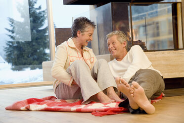 Mature couple sitting in front of fireplace - WESTF07748