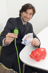 Mann hält grünen Stecker und Geldscheine - WESTF07490