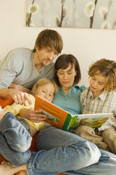 Family reading story book in living room - WESTF07277