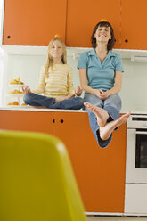 Mutter und Tochter (8-9) in der Küche, Orange auf dem Kopf balancierend, lächelnd, Porträt - WESTF07248