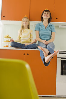 Mother and daughter (8-9) in the kitchen, balancing orange on head, smiling, portrait - WESTF07248
