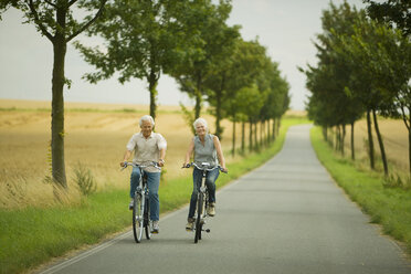 Senior couple biking on country road - WESTF07185