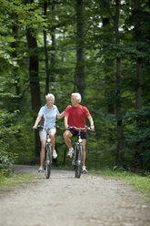 Senior couple biking on forest track - WESTF07140