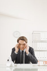 Businessman sitting at desk, hands to head - WESTF07833