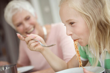Girl (8-9) eating spaghetti, grandmother in background - HKF00209