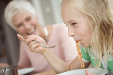 Mädchen (8-9) isst Spaghetti, Großmutter im Hintergrund - HKF00209