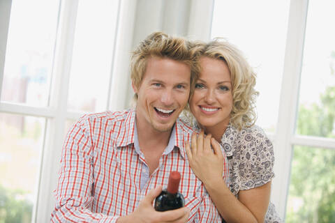 Young couple holding wine bottle, smiling, portrait stock photo