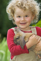 Blondes Mädchen (4-5) mit lockigem Haar hält Kaninchen, Porträt - SHF00211