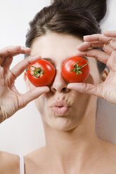 Brunette woman covering eyes with tomatoes, portrait - MAEF00948