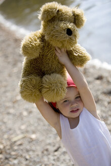 Germany, Bavaria, Ammersee, little girl (3-4) lifting teddy bear - JUF00006