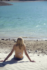 Italy, Blond girl relaxing on beach, rear view - JUF00001