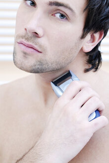 Young man using electric razor, portrait - VRF00064