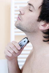 Junger Mann mit elektrischem Rasierapparat, Porträt - VRF00063