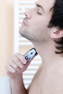 Young man using electric razor, portrait - VRF00063