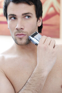 Young man using electric razor, portrait - VRF00062