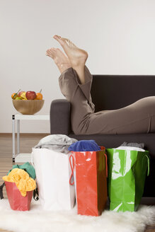 Frau entspannt auf Sofa, Einkaufstüten im Vordergrund - LDF00588