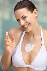 Young woman applying moisturizer to her body, smiling, portrait - ABF00206