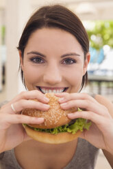 Asia, Thailand, Young woman eating hamburger, smiling, close-up, portrait - RDF00604