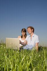 Germany, Bavaria, Young couple in meadow, using laptop, portrait - RDF00557