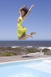 South Africa, Cape Town, Young woman jumping by swimmingpool, arms raised - ABF00383