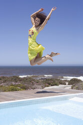 Südafrika, Kapstadt, Junge Frau springt mit erhobenen Armen durch den Swimmingpool - ABF00383