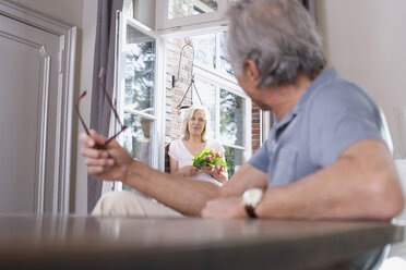Älterer Mann sitzt am Tisch, ältere Frau steht in der Tür, Porträt - WESTF08226