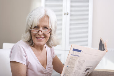 Senior woman holding newspaper, smiling, portrait - WESTF08210