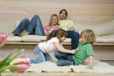 Junge (8-9) und Mädchen (6-7) kämpfen auf einem Teppich, Eltern im Hintergrund, Porträt - WESTF08129
