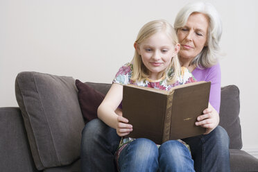 Großmutter und Enkelin (8-9) lesen ein Buch auf dem Sofa, Porträt - WESTF08339
