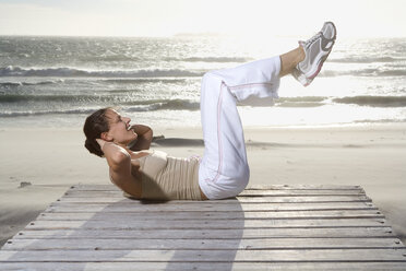 Junge Frau macht Sit-Ups am Strand - ABF00280